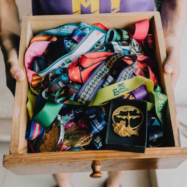 Hands holding a wooden drawer full of race medals and lanyards
