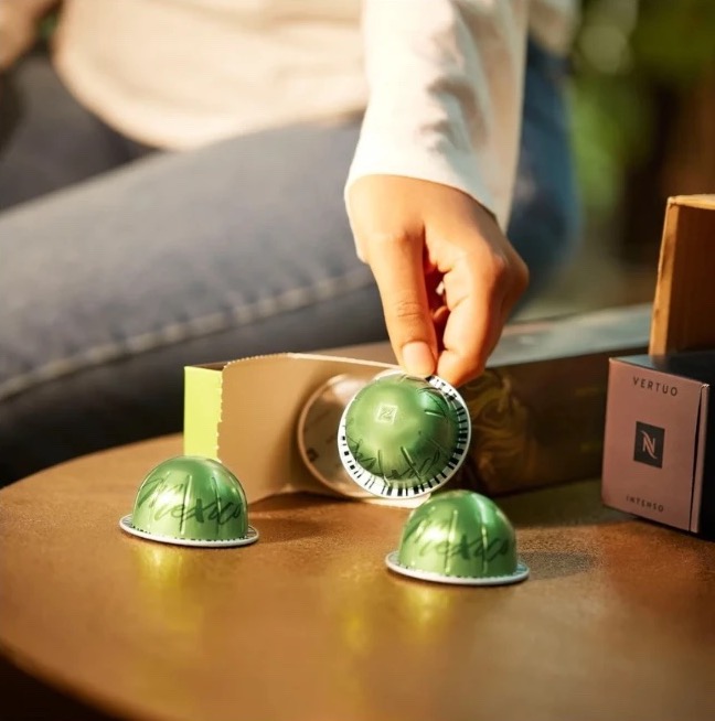 A hand placing green Nespresso Vertuo capsules on a wooden table