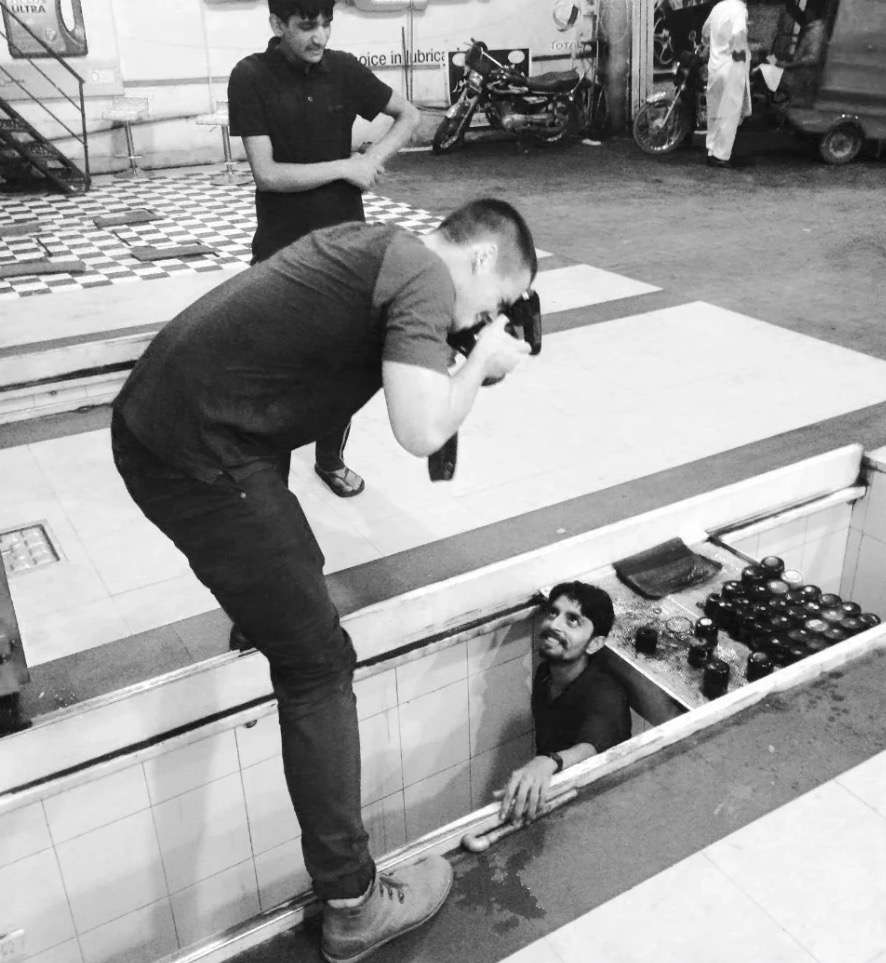 Sam photographing a mechanic working in an inspection pit at a truck stop in Pakistan